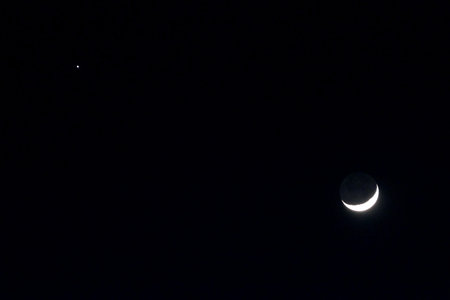 Crescent moon seen in a night sky with a single star in the distance