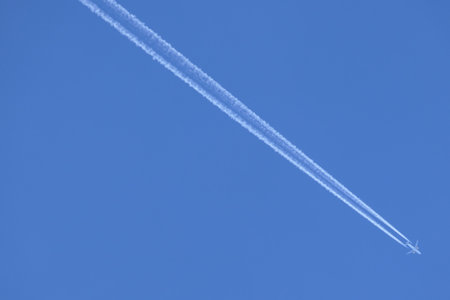 Contrail trail from a flying jet aircraft bisecting a beautiful blue skyの写真素材
