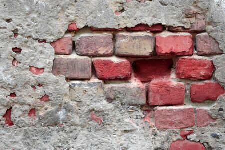 Old ruined wall with sticking out fragments of red bricks and cementの写真素材