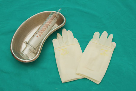 Glass syringe in  sterile basin and  latex glove for tube feeding diet