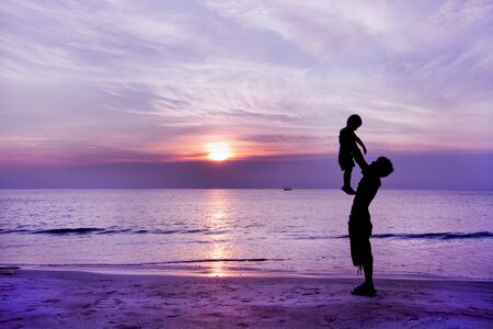 Happy family having fun on the beach,Father and son play on the Beach in sunrise silhouette shotの写真素材