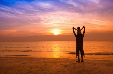 silhouettes of father and son on sunrise sea background,family conceptの写真素材