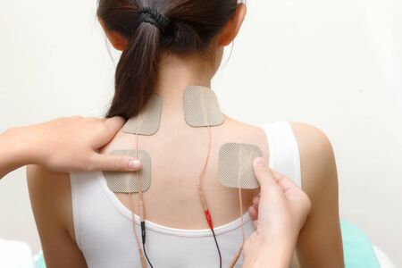 Closeup of therapist placing electrodes on woman's backの写真素材