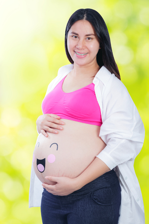 Happy pregnant woman with smiley face on her bellyの写真素材