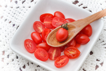 Fresh red tomatoes on a wooden spoon in white bowlの写真素材