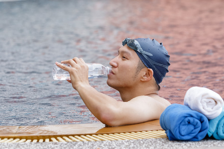 Asian swimmer is drinking water in the pool, after swimmingの写真素材