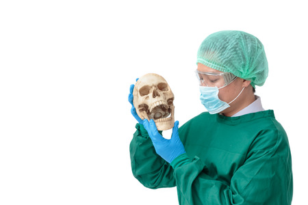 Asian surgeon man with protective clothing holding an artificial human skullの写真素材