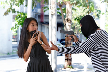 Dangerous man thief in black hoodie threatening with gun to scared young woman on the streetの写真素材
