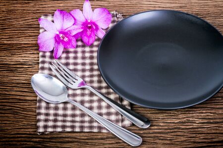 Plate, spoon and fork at napkin with orchid flower on wooden backgroundの写真素材