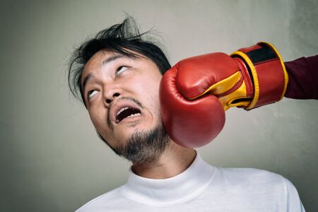 funny face man getting punch in face with boxing glove against gray backgroundの写真素材