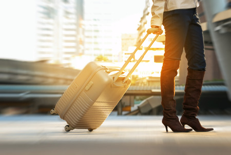 Woman pulling suitcase walking along sidewalk outdoors in city,Tourist walking in the urban city  の写真素材