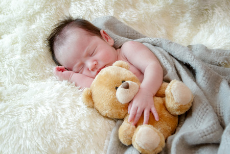 Cute newborn baby girl sleeps with a toy teddy bearの写真素材