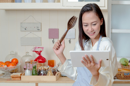 Asian woman is cooking in the kitchen with digital tablet of recipe.の写真素材