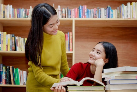 Two happy Asian college student reading books in the library togetherの写真素材