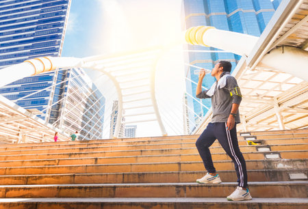 Man in sportswear drinking water from bottle after work in front of urban buildings