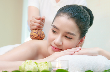 Young Asian woman having Thai herbal compress massage in spa environment.の写真素材