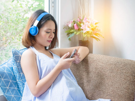 Pregnant woman use mobile smart phone while sitting in bed and relaxing,Pregnancy and technologyの写真素材