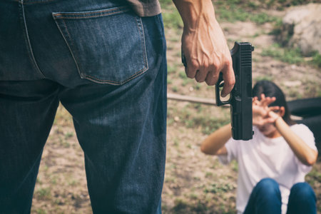 Bandit man holding gun standing in front of young woman victim feeling fear 