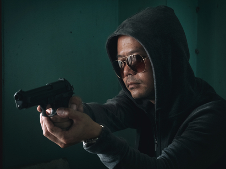 Hooded man with a gun in the dark roomの写真素材
