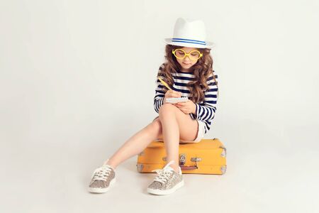 Girl is is sitting on a suitcase and writingの写真素材