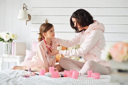 Young mother is fixing jewelry on her daughters neckの写真素材