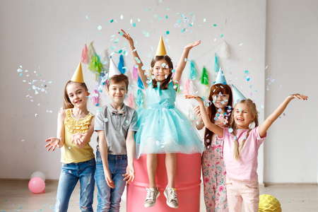 Adorable kids have fun together, throw colourful confetti, wears cone hats, have fun at birthday party, play together in different games, spend time in decorated room. Children and events conceptの写真素材