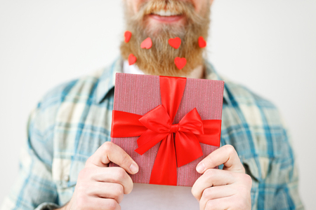 Cropped shot of romantic bearded male holds present box in front, going to make surprise for girlfriend, isolated on white background. Unrecognizable fashionable young guy with wrapped gift boxの写真素材
