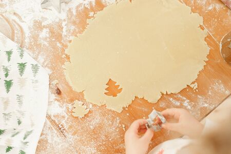 Child s hands make cookies from dough, uses cookie cutter in shape of firtree, prepares for winter holidays, bakes delicious dessert on Christmas, helps parents. Kid cutts out shapes from pastry.の写真素材