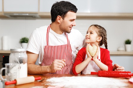 Portrait of handsome affectionate father embraces her little daughter, make cookies together, being in good mood. Domestic atmosphere. Baking concept. Friendly family. Childhood concept.の写真素材