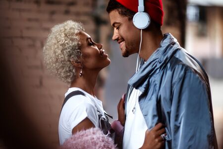 Happy Afro American man in headphones and his female friend with curly hairdo stand close to each other.の写真素材