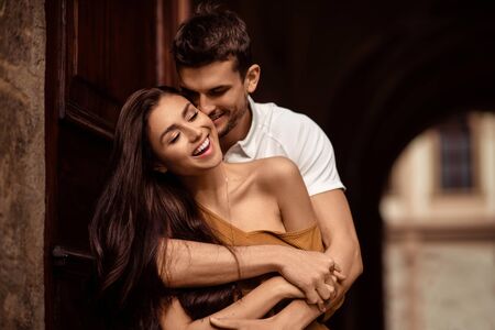 Happy young female with long dark hair glad to recieve passionate kiss from her boyfriend. Handsome male embraces his girlfriend and kisses. Portrait of lovely young couple express mutual love.の写真素材