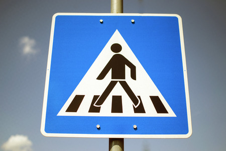 Blue pedestrian crossing sign against blue skyの写真素材