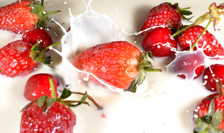 Red Strawberries and Cherries dropping into milkの写真素材