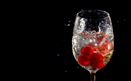 Cherries and Strawberry dropped into glass of water on isolated black backgroundの写真素材