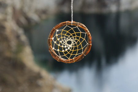 Handmade dream catcher on background of rocks and lake. Tribal elements