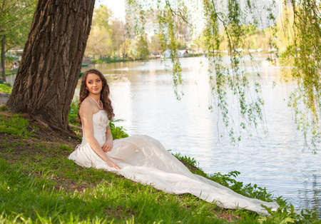 Fantasy portrait of elegant bride in white wedding dress sitting near riverの写真素材