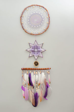 Closeup star mandala dreamcatcher with purple white feathers and cinnamon stick on gray background