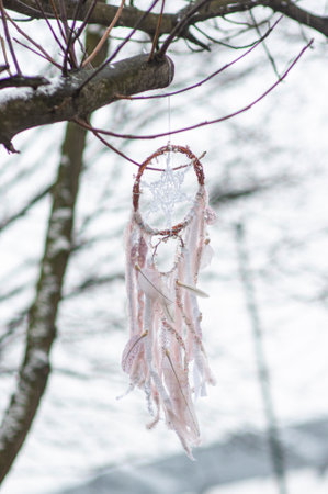 Handmade white dreamcatcher with lace, feathers close up tribal bohemian craft tree hanging outdoors, winter weather wind, rain and snowの写真素材