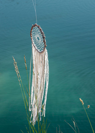 Handmade dreamcatcher close up tribal bohemian craft hanging over the azure lake outdoorsの写真素材