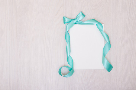 Creative mock up with ablank piece of paper. blue ribbon and bow. Empty sheet of paper.の写真素材