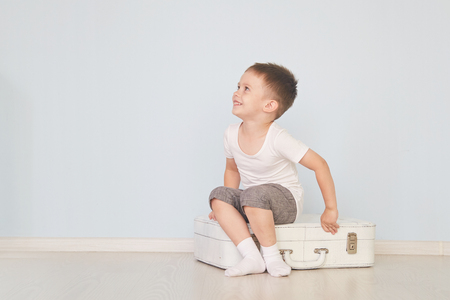 the boy sits on the white suitcase in the roomの写真素材