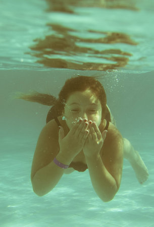The little girl in the hotel pool swimming underwater and smiling without googlesの写真素材