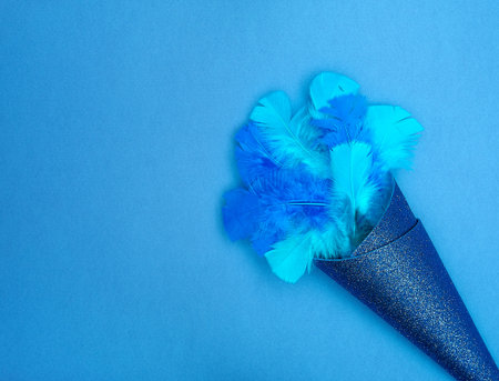 Two-tone blue feathers in glittery blue paper on a bright blue background. Text space. Celebrations, birthday parties, communication, self-expression, concept. Minimal style. Top view. Flat lay.の写真素材