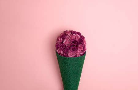 Bouquet of artificial purple roses in green glittering paper on a pastel pink background. Text space. Celebrations, Valentine's Day, weddings. Minimal style. Top view. Flat lay.の写真素材