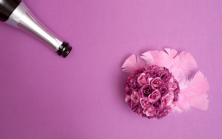 Bouquet of artificial purple roses with pink feathers, a bottle of sparkling wine on a purple...