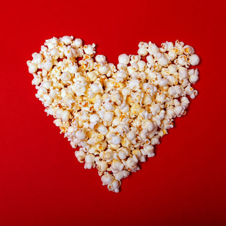 Popcorn heart on a flat red background. Top view. Valentine's Day, cinema time concept. Minimal style.の写真素材