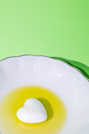 Plate, white. A little white heart in oil on a plate. Harsh shadow. Green background. Cooking, health, fresh, organic, concept. Minimal style.の写真素材
