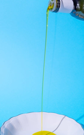 Plate, white. Oil leaking from the bottle into the plate. Blue background. Text space. Cooking,...