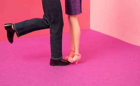 A woman's shoe stands on a man's shoe. The other man's leg is raised backwards. Dolls on a purple-pink background. Text space. Love, relationships, concept. Minimal style.の写真素材