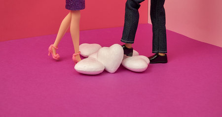 A woman and a man walk towards each other over a pile of white hearts. Dolls. Fuchsia, red, pink...
